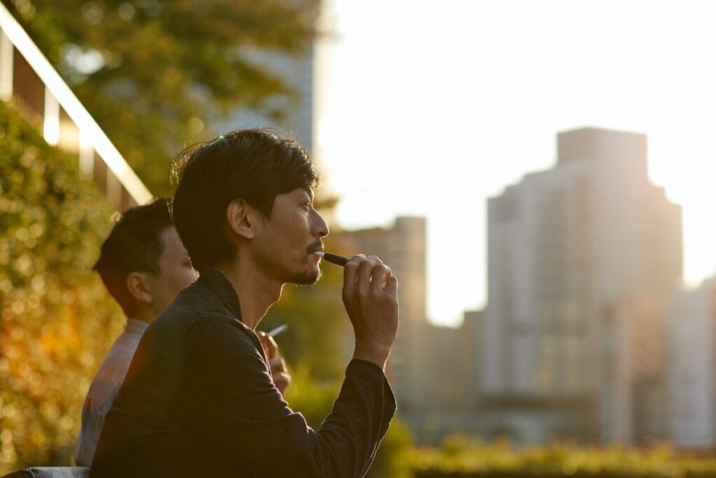 Man hits vape pen in a city park at sunset.