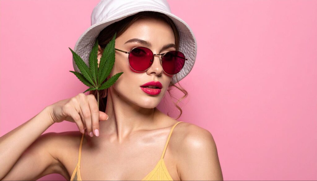 Modern woman holding a cannabis hemp leaf next to her face.